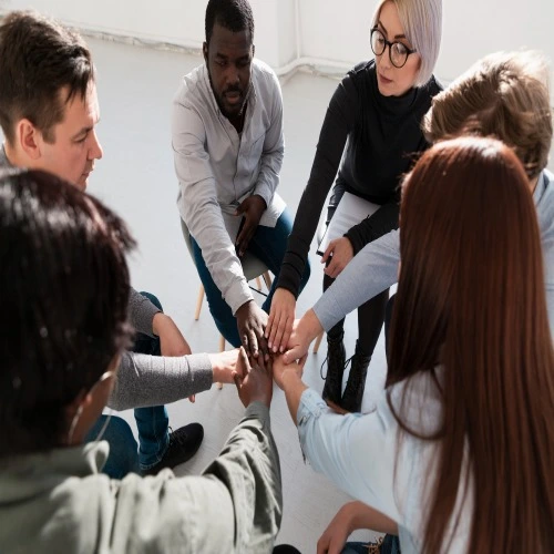 Diverse trauma support group members placing hands together in unity during a therapy session in Orlando FL