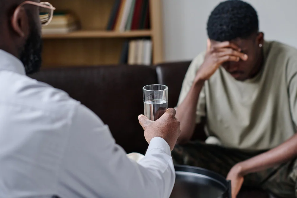 Compassionate therapist handing a glass of water to a distressed patient during a substance abuse consultation at BCSS
